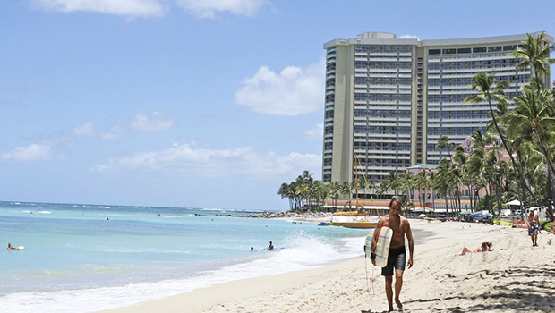 Man walking on Waikiki beach with hotel in the background.