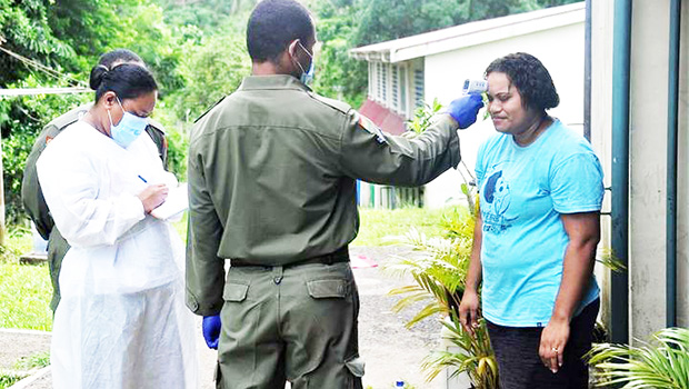 Soldier taking temperature of a woman in order to screen for COVID.