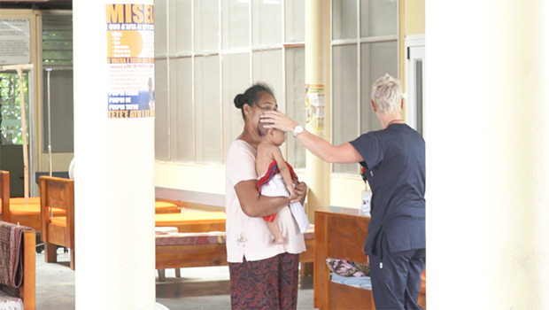Mother holding baby as doctor touches its head