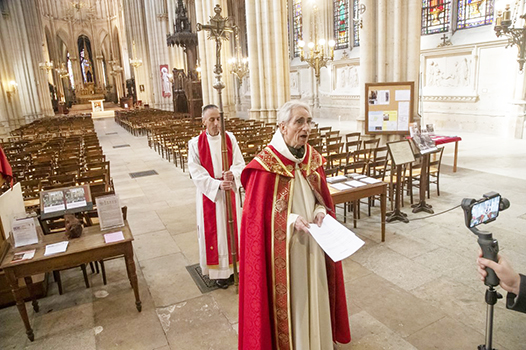 Priest Edouard Dacre-Wright, left, holds the processional cross as priest Marc Lambert speaks to a video camera during the Way of the Cross ceremony