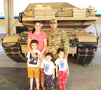 DeAngelo Herrera and family posing in front of a tank