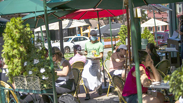 A waiter in a face mask delivers food to the tables outside of a restauran