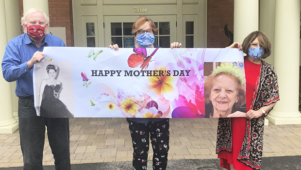 Three siblings wearing cloth face masks with a Happy Mother's Day sign
