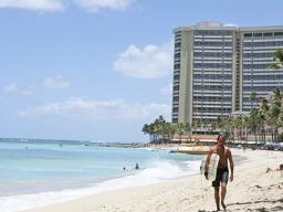 Man walking on Waikiki beach with hotel in the background.