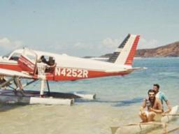 A Cherokee 6 on floats with a small paopao with 2 people in it beside the aircraft.