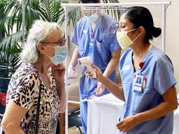 Patient at entrane to Queens hospital with nurse taking temp.