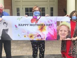 Three siblings wearing cloth face masks with a Happy Mother's Day sign
