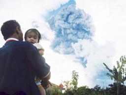 In this Sunday, June 9, 2019, file photo, a man carrying a child watches Mount Sinabung spew volcanic material into