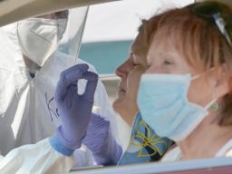 A woman sitting in a car administers a swab to her nose.