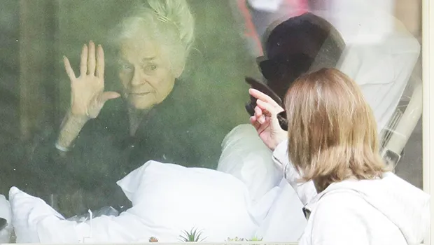 Judie Shape, left, who has tested positive for the coronavirus, waves to her daughter, Lori Spencer