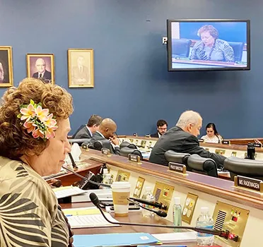 Congresswoman Amata speaking into microphone in committee room.