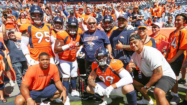 The defensive line group — Derek Wolfe (95), Shelby Harris (96), Zach Kerr (92), Domata Peko Sr. (94), Kyle Peko (90), DeMarcus Walker (57) and Adam Gotsis (99) — take a group photo with Peko Sr.'s father