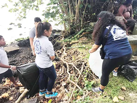 Students remove debris from along the shoreline of the Pala Lagoon