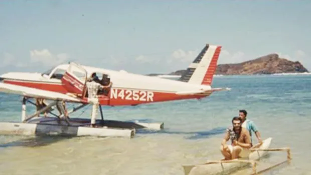 A Cherokee 6 on floats with a small paopao with 2 people in it beside the aircraft.