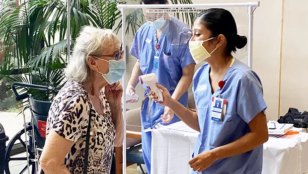 Patient at entrane to Queens hospital with nurse taking temp.