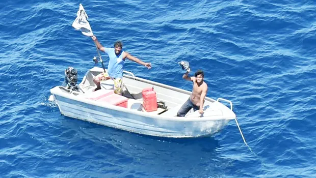 Two men in small boat waving overhead at airplane unseen in photo