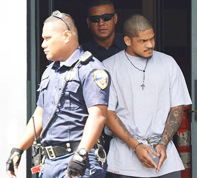 Manu Lefatia in handcuffs escorted by two police officers