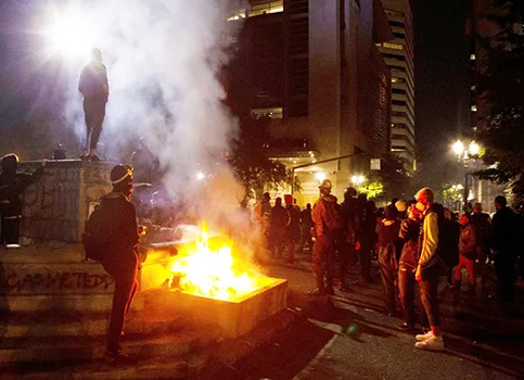 In this July 4, 2020, file photo, protesters gather near a fire in downtown Portland, Ore