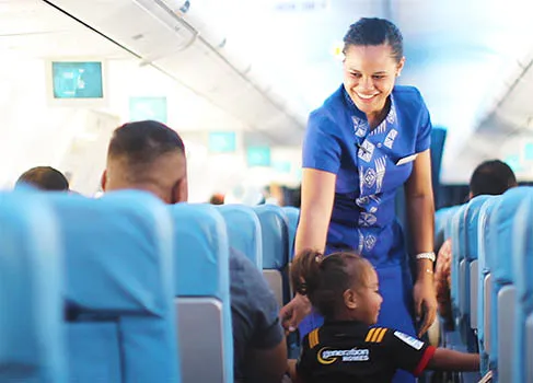 Samoa Airways flight attendant talking with a child on the airplace while another passenger looks on.