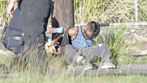 robbery suspect sitting in grass being handcuffed
