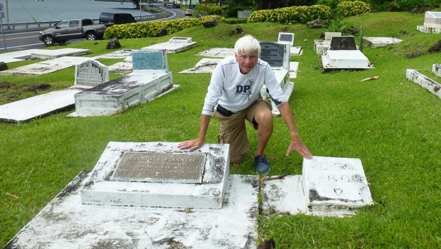 Tom Blake touches the two gravestones in Pago Pago, of his friend Mark Flannery’s parents