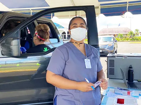 Healthcare worker with mask standing beside a car
