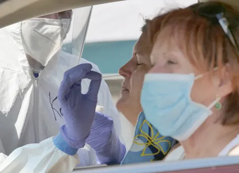 A woman sitting in a car administers a swab to her nose.